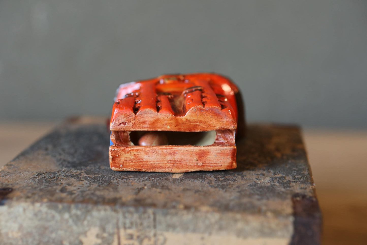 A red wooden object with a carved design sits on a metal surface against a gray background.
