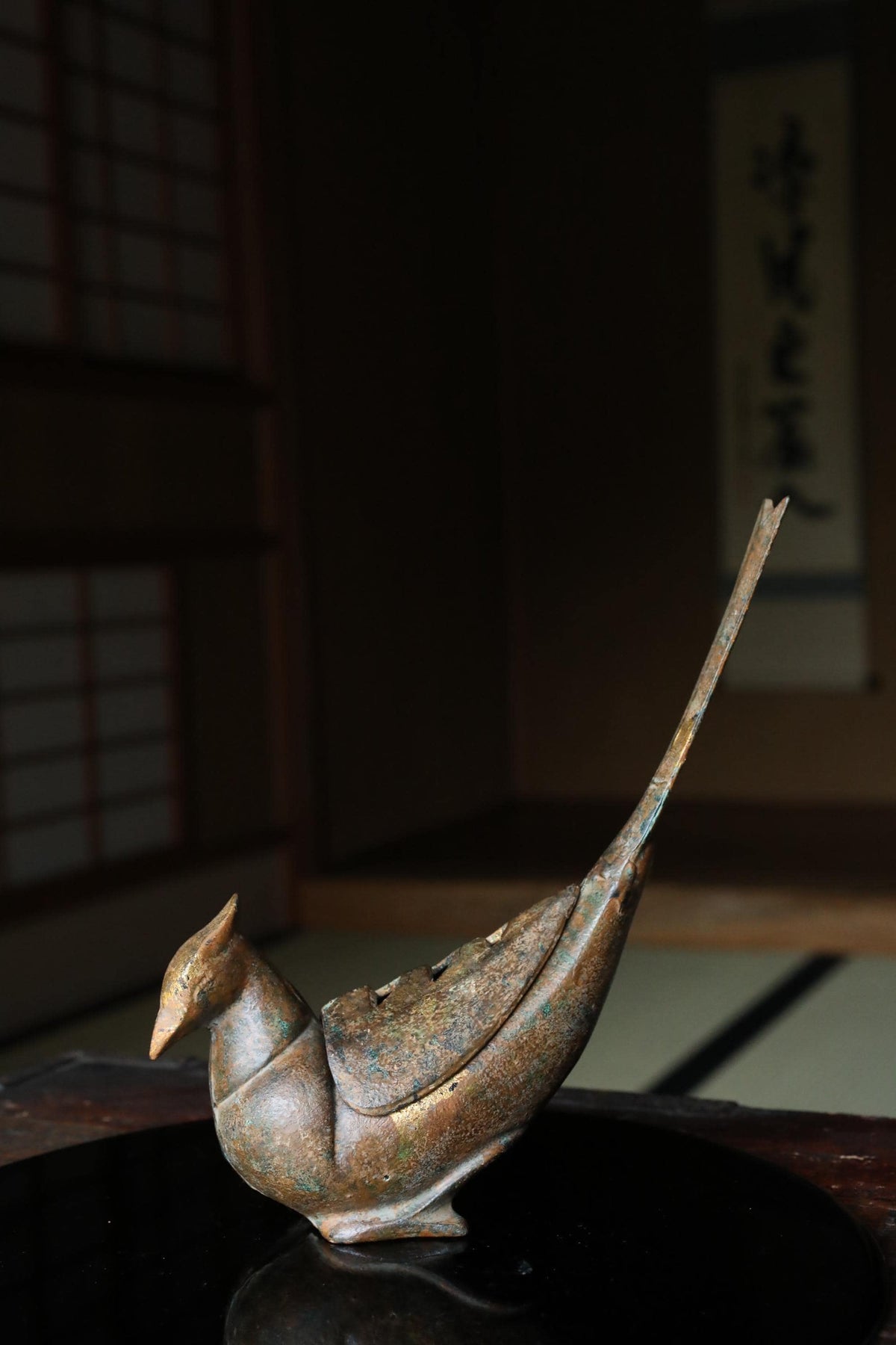 a bronze bird figurine sitting on a reflective surface.