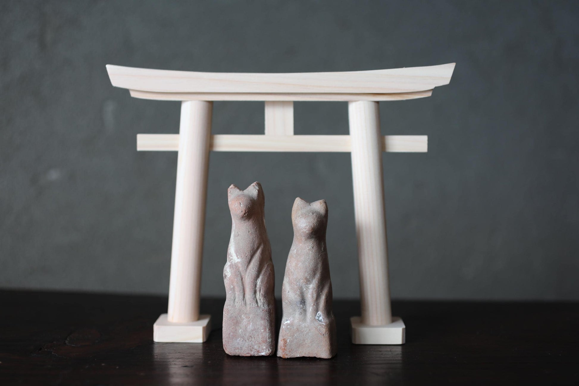 two small stone statues of cats standing in front of a wooden torii gate.