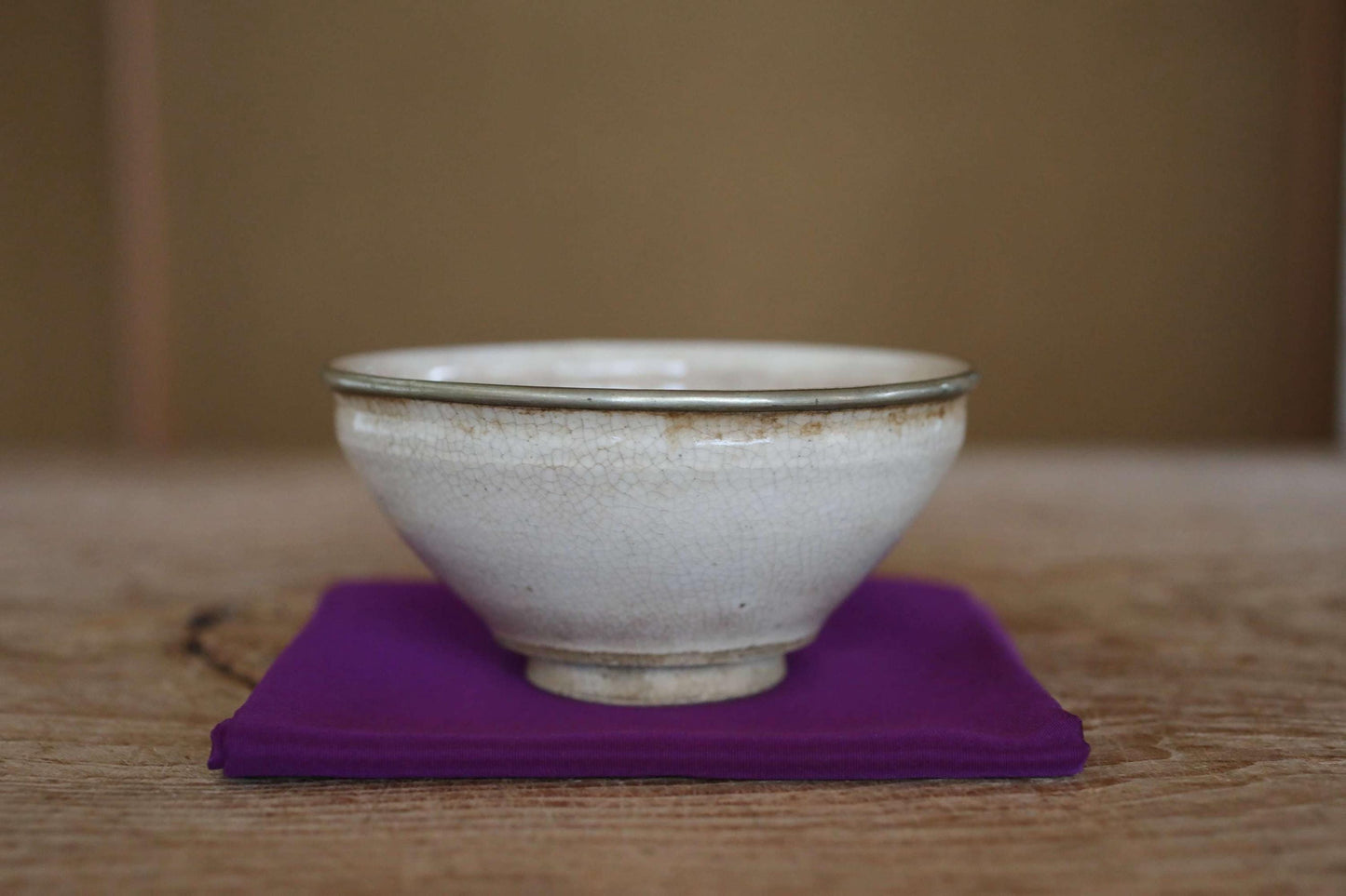 A white ceramic bowl with a green rim sits on a purple cloth on a wooden surface.