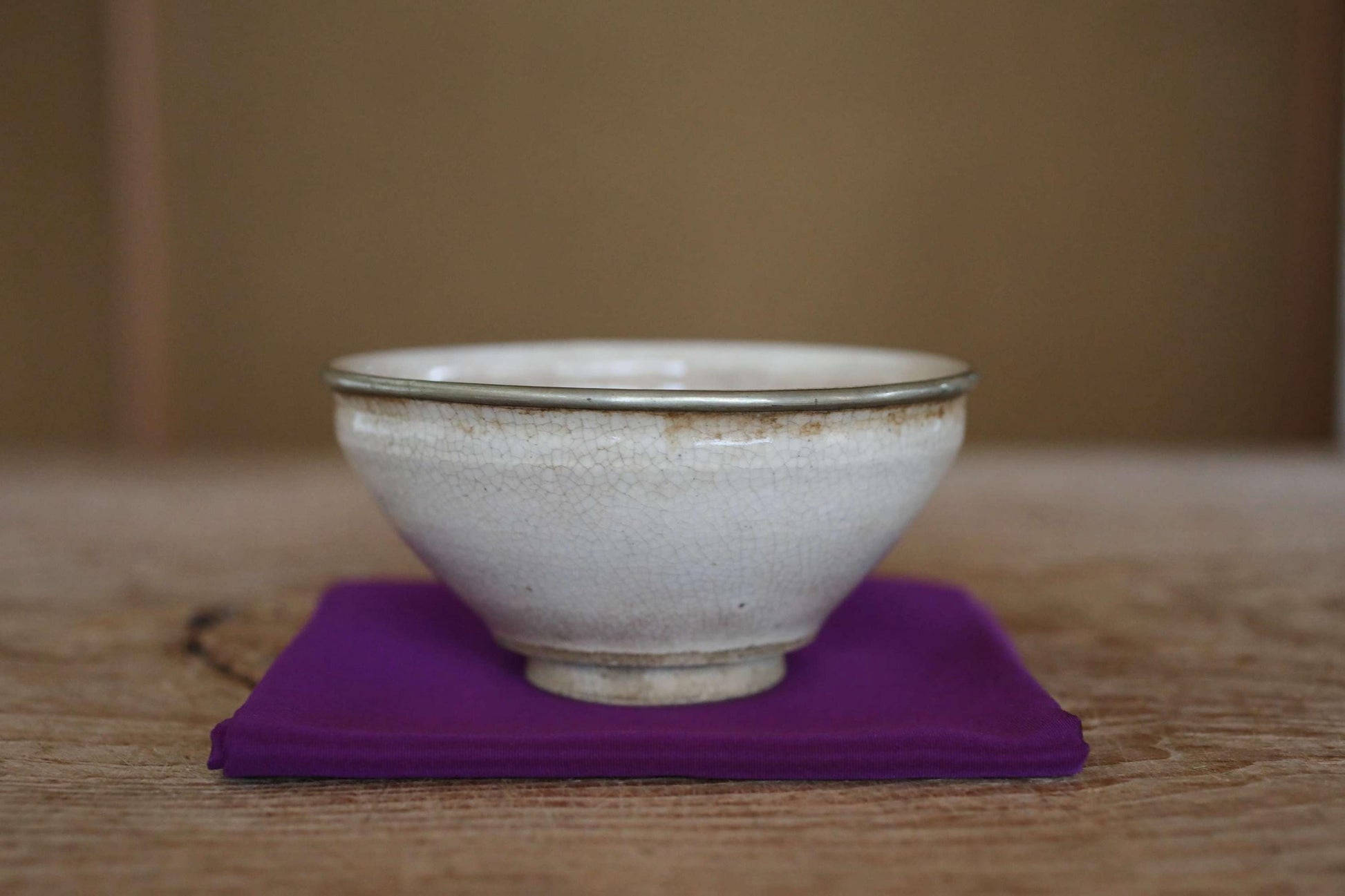 A white ceramic bowl with a green rim sits on a purple cloth on a wooden surface.