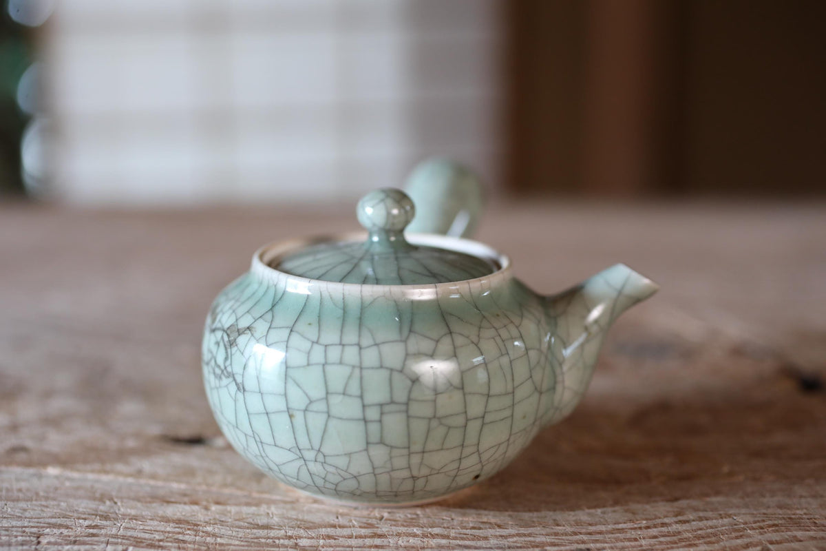 A ceramic teapot with a cracked, green-colored exterior sits on a wooden surface.