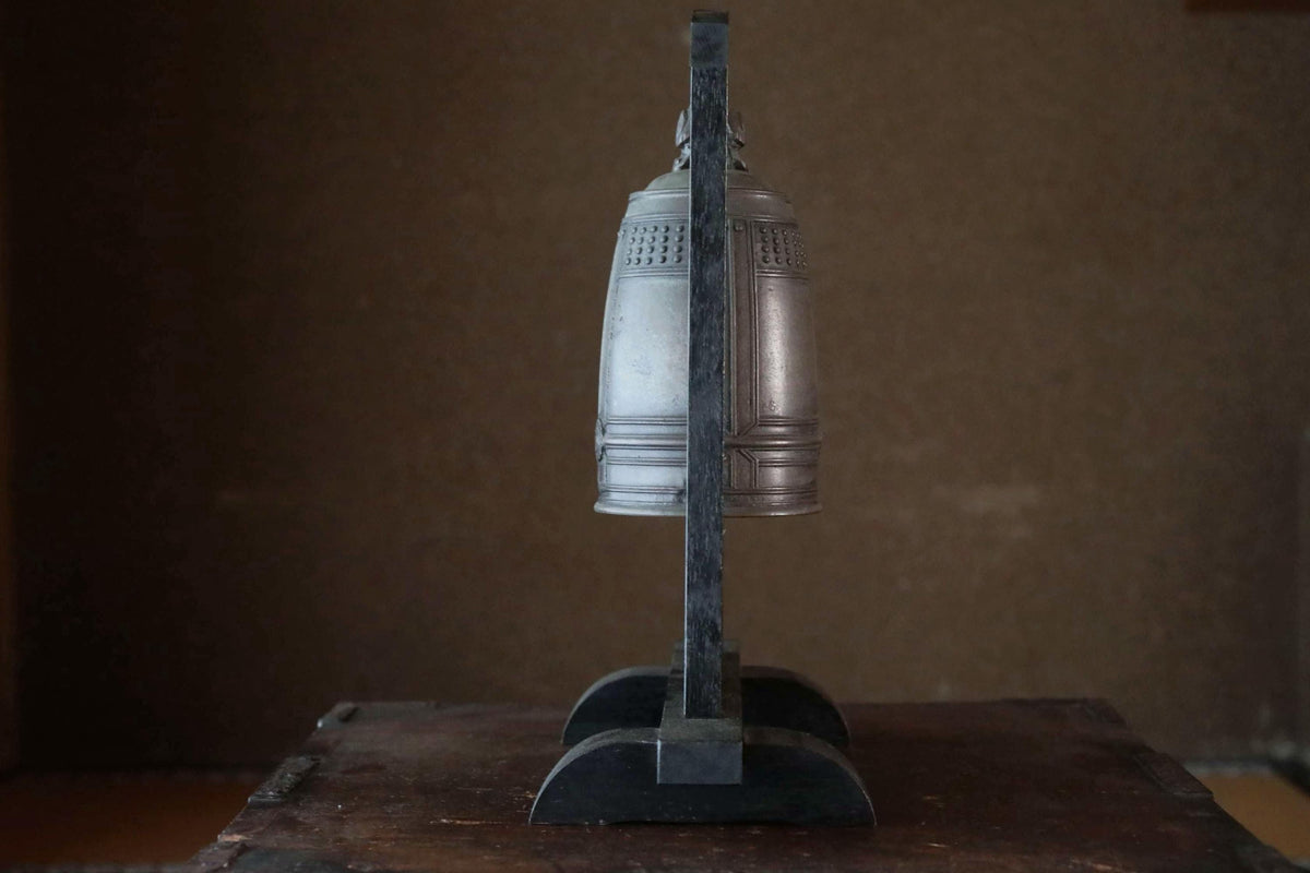 A silver bell is mounted on a black stand, positioned on a wooden surface.