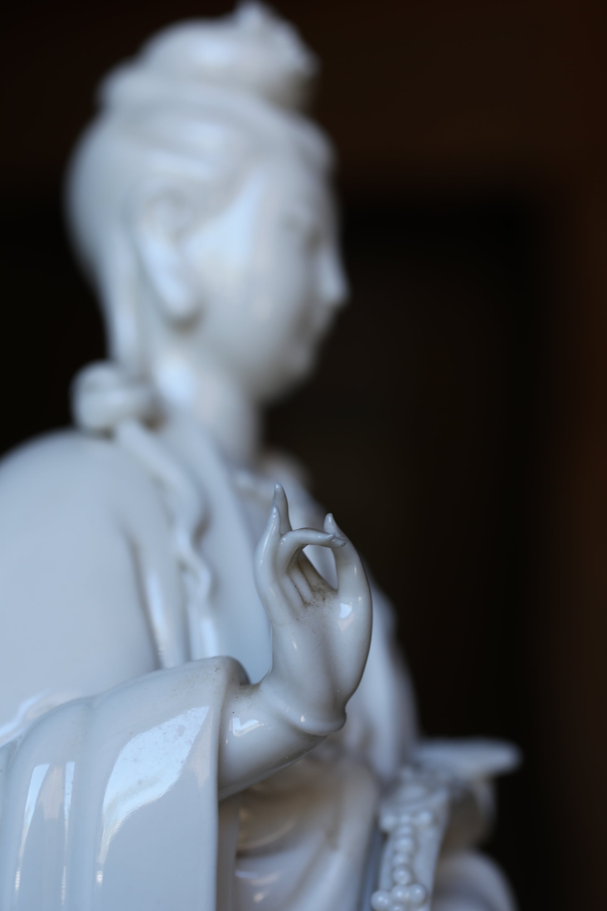 A close-up view of a white ceramic sculpture depicting a human figure with outstretched arms, set against a dark background.