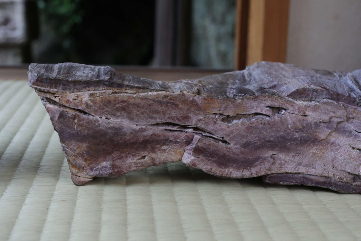 a close-up view of a large, irregularly shaped rock or stone with a dark purple or purple-like hue. The rock appears to be made of a material that resembles wood or stone, and it is resting on a textured surface, possibly a mat or a woven material.