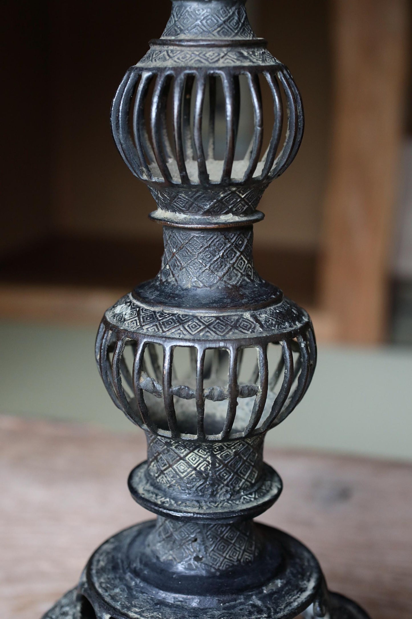 A close-up view of an ornate, decorative metal lamp with a tall, cylindrical base and a series of smaller, domed or rounded elements.