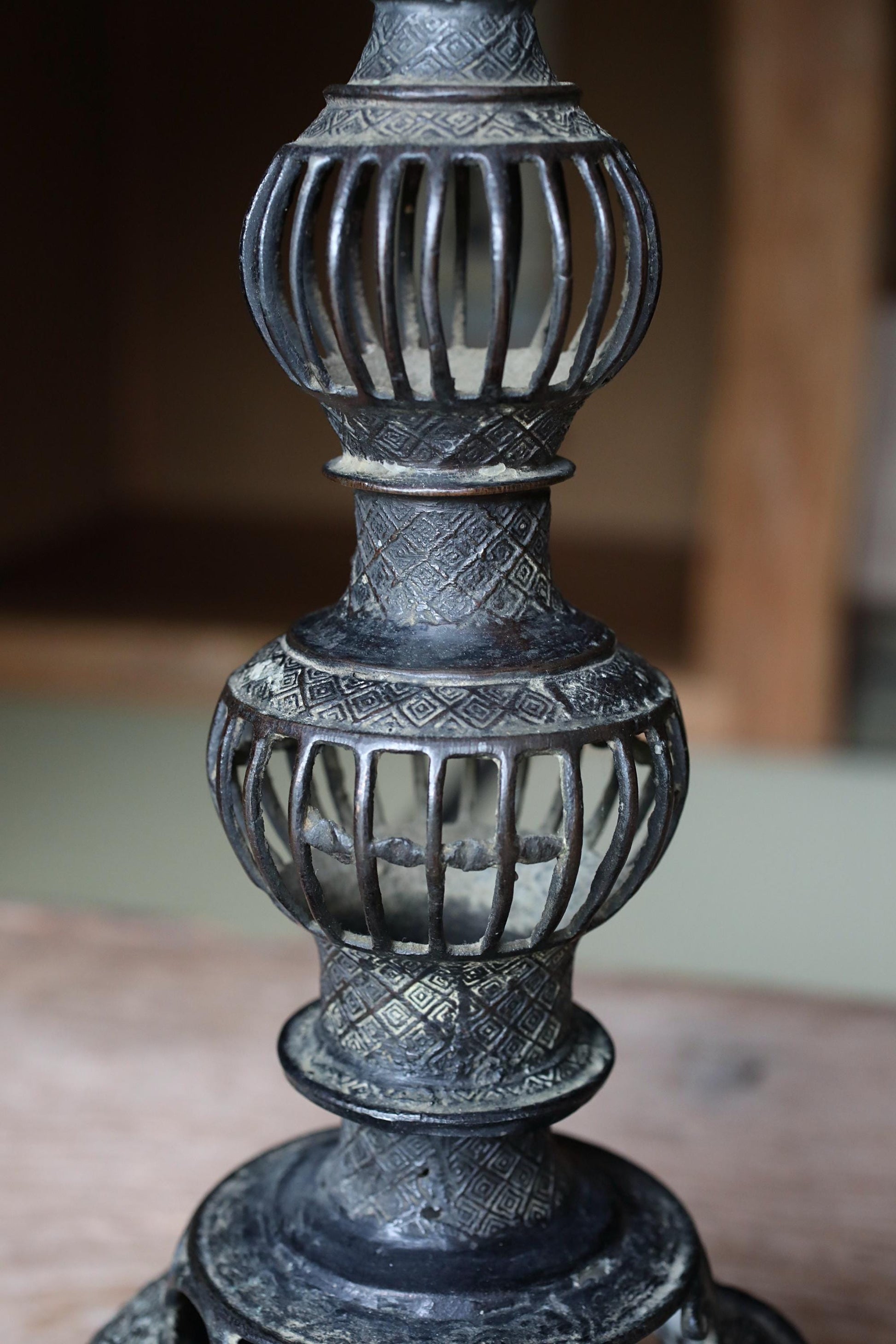 A close-up view of an ornate, decorative metal lamp with a tall, cylindrical base and a series of smaller, domed or rounded elements.