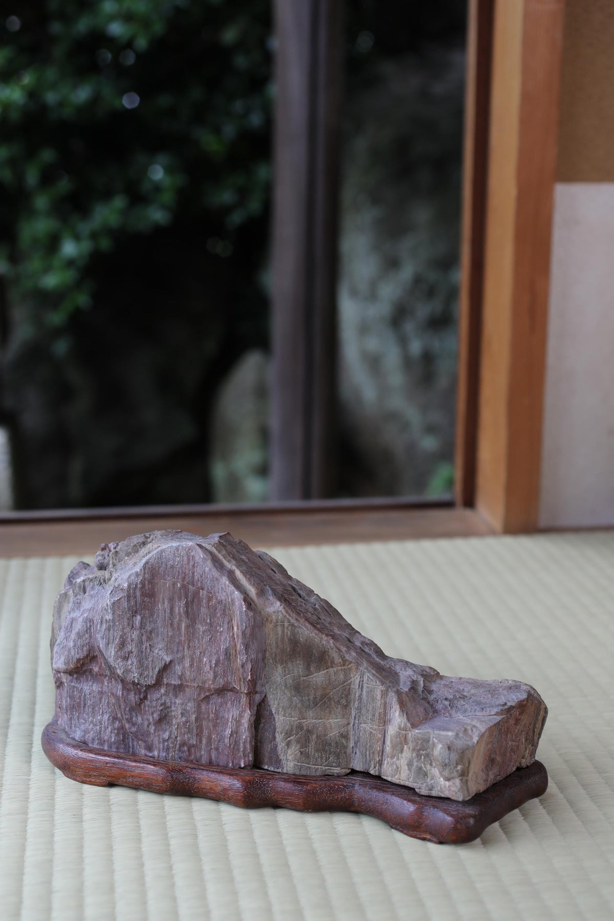 a large, jagged rock sitting on a wooden base, placed on a woven mat.