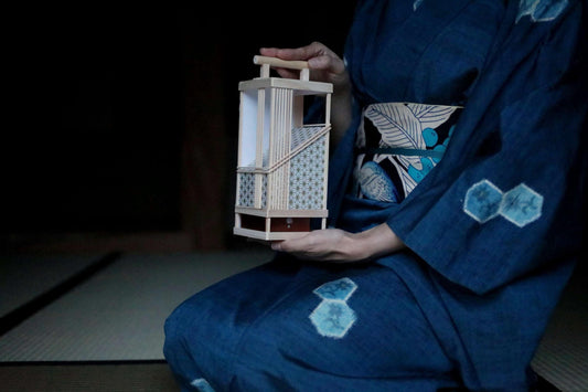 A person wearing a blue kimono with a wooden lantern in their hands.