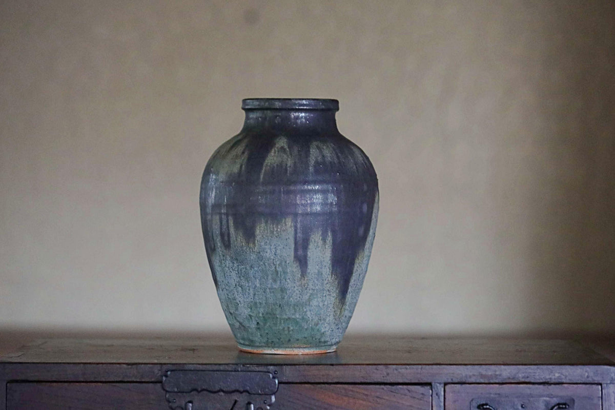 A dark blue ceramic vase with a textured surface sits on a wooden surface against a plain background.