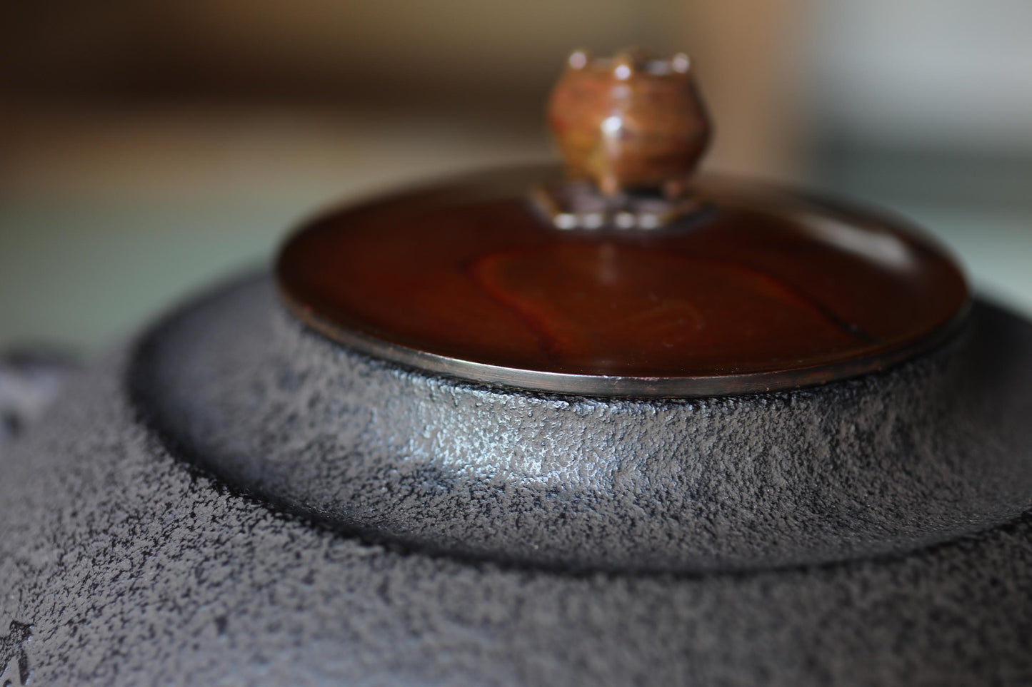 A close-up image of a dark-colored ceramic teapot with a brown lid and a small decorative object on top.