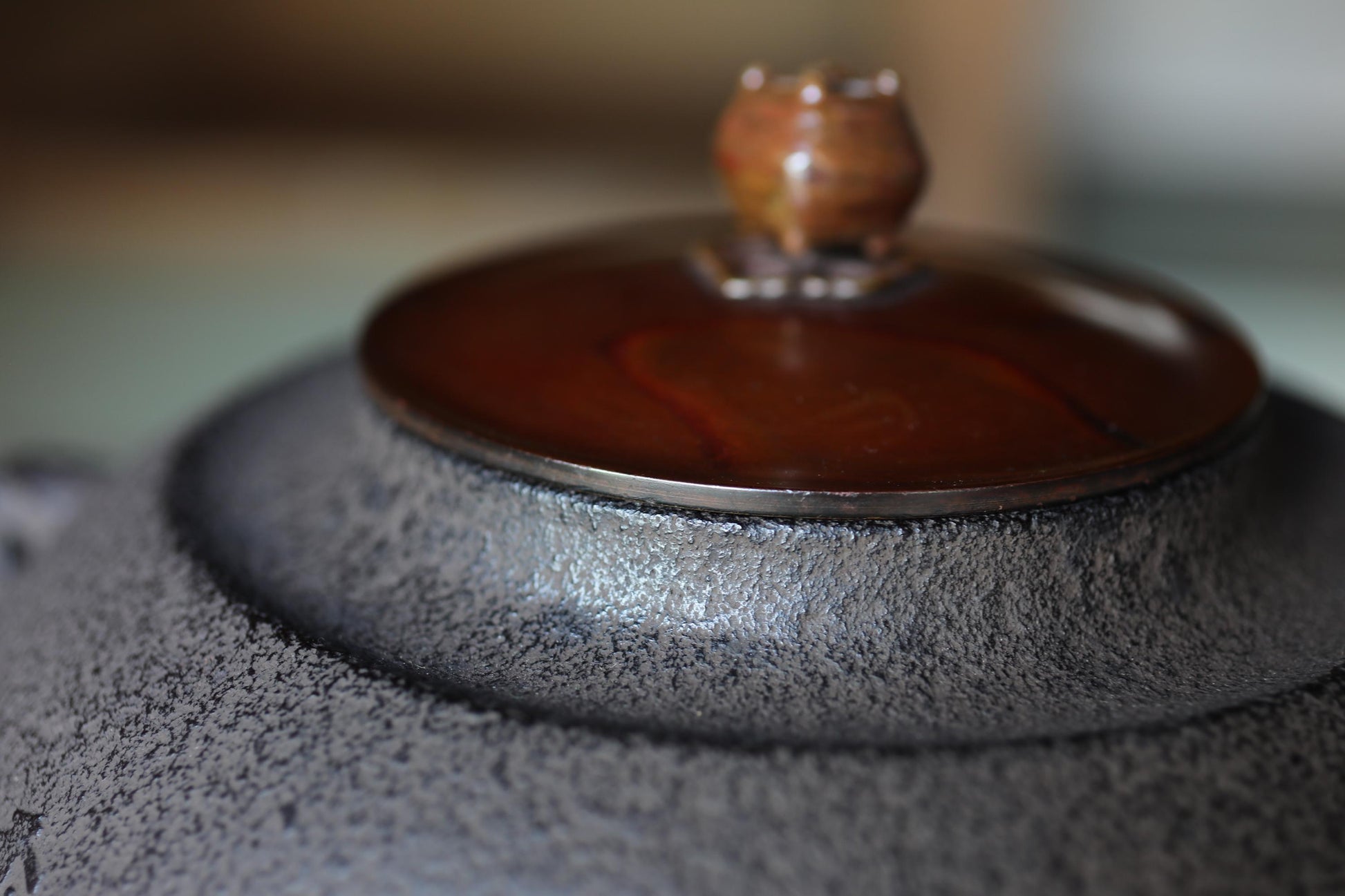 A close-up image of a dark-colored ceramic teapot with a brown lid and a small decorative object on top.