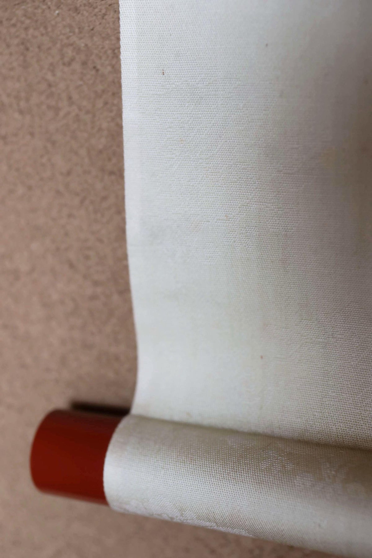 A close-up view of a white fabric roll with a red end, resting on a wooden surface.