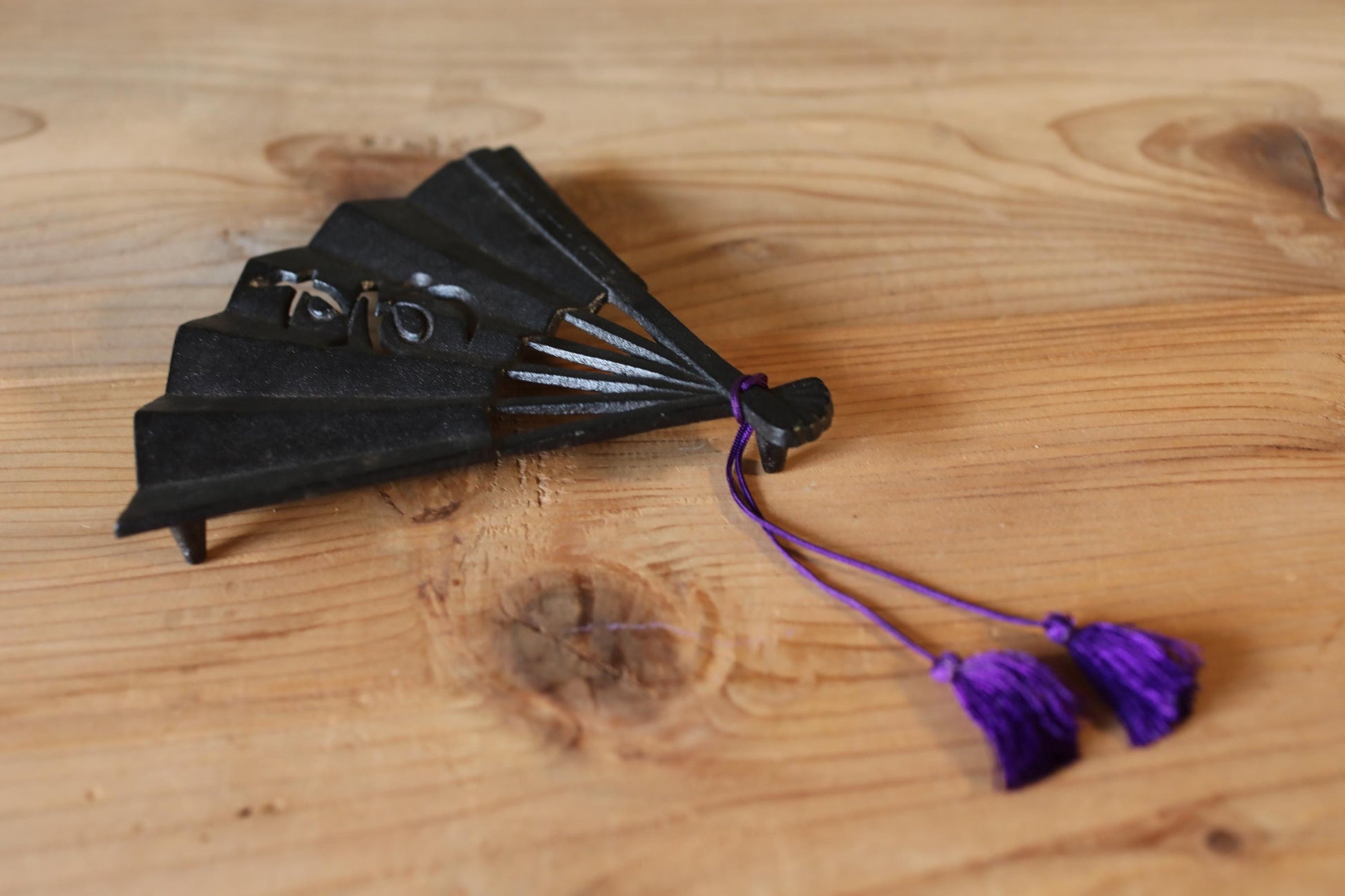 A black metal fan with purple tassels is placed on a wooden surface.