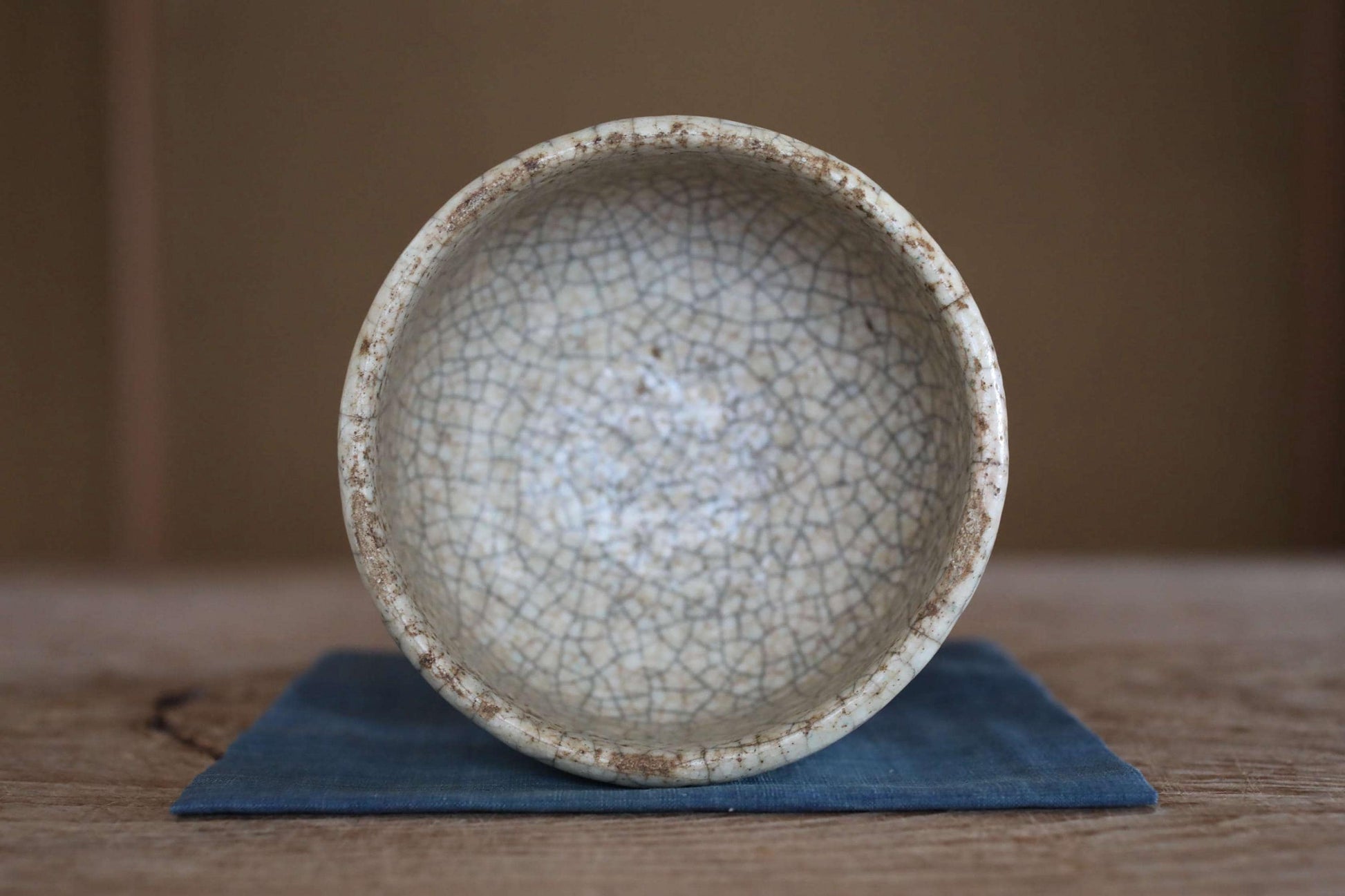 A white ceramic bowl with a textured surface sits on a blue cloth on a wooden surface.