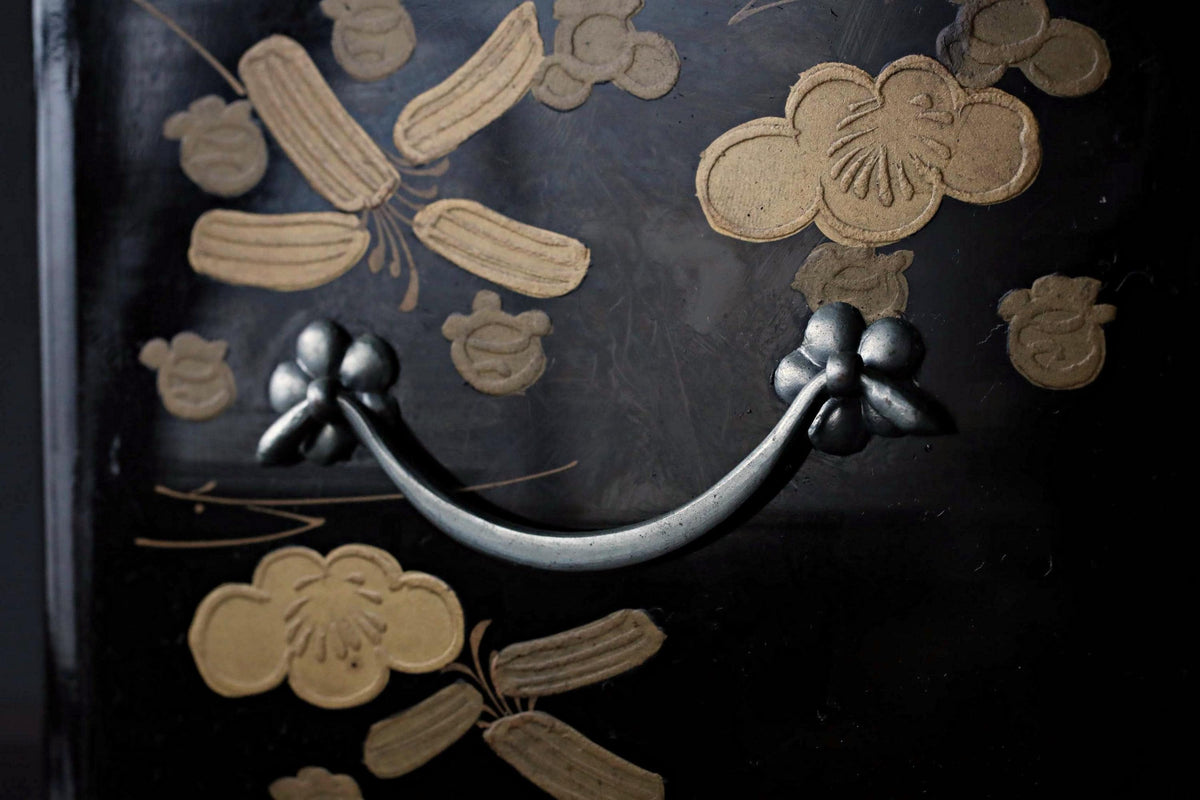 a close-up view of a decorative metal handle on a black surface, with intricate floral designs in gold and brown tones.