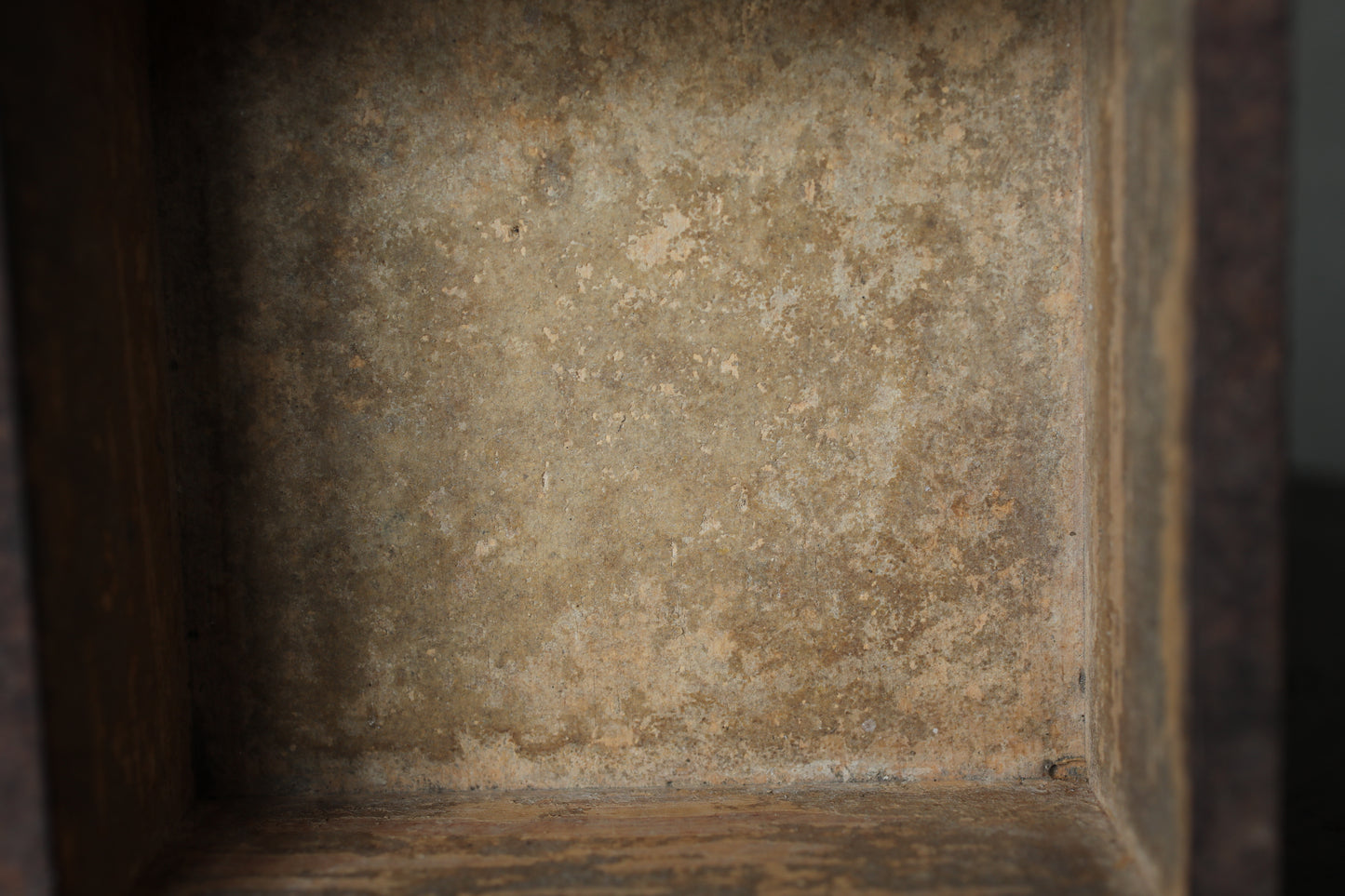 a close-up view of a weathered, textured surface, possibly a wall or a piece of furniture, with a rough, aged appearance.