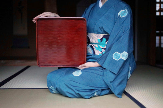 A person wearing a traditional Japanese kimono is holding a red tray.