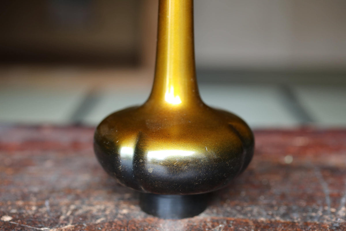 A close-up image of a shiny gold-colored vase or sculpture with a dark, textured base.