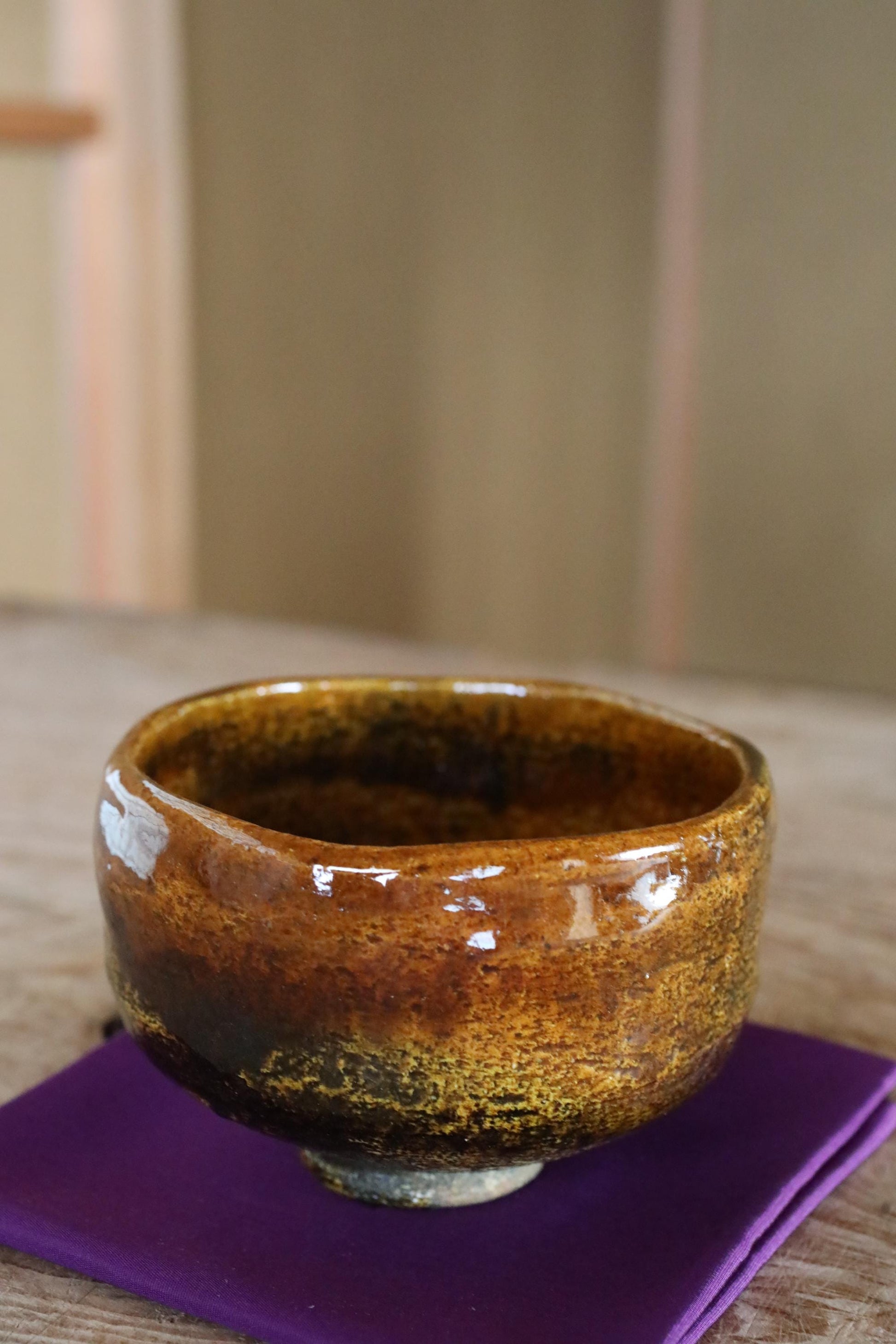 A ceramic bowl with a brown glaze sits on a purple napkin on a wooden surface.