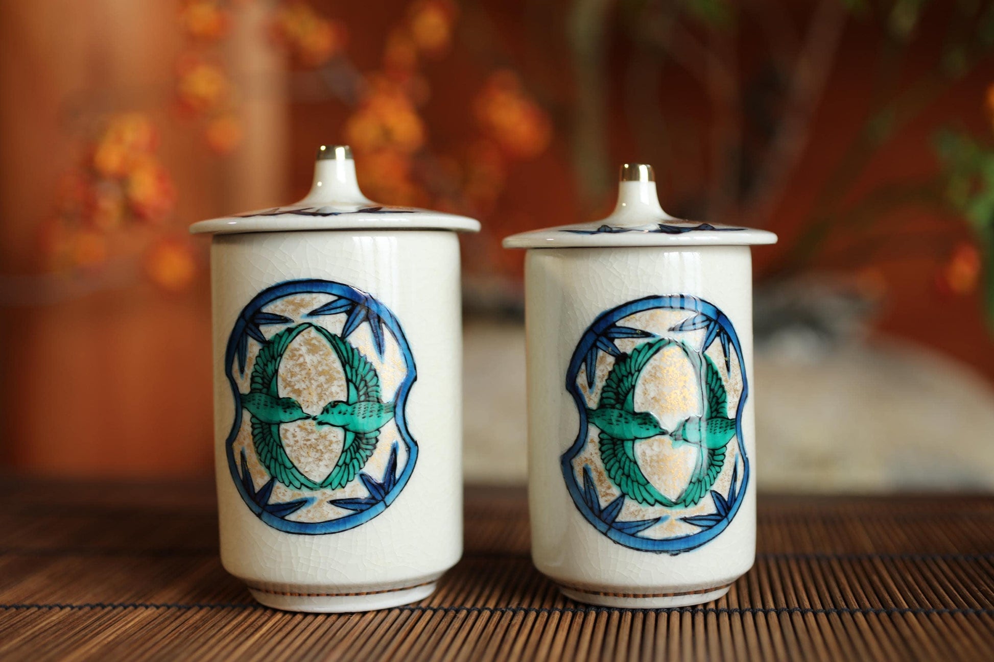 Two white ceramic containers with blue and green designs, featuring a bird motif, are placed on a wooden surface.