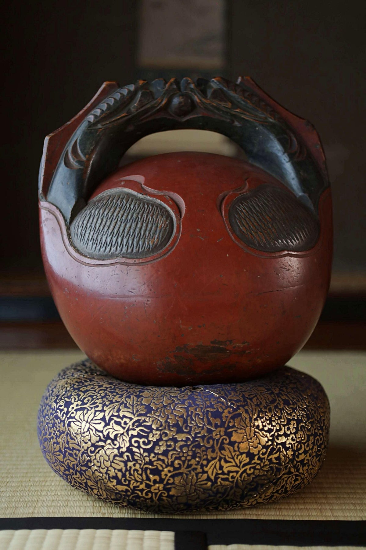 A red ceramic bowl with a black handle and decorative elements, placed on a blue and gold decorative object.