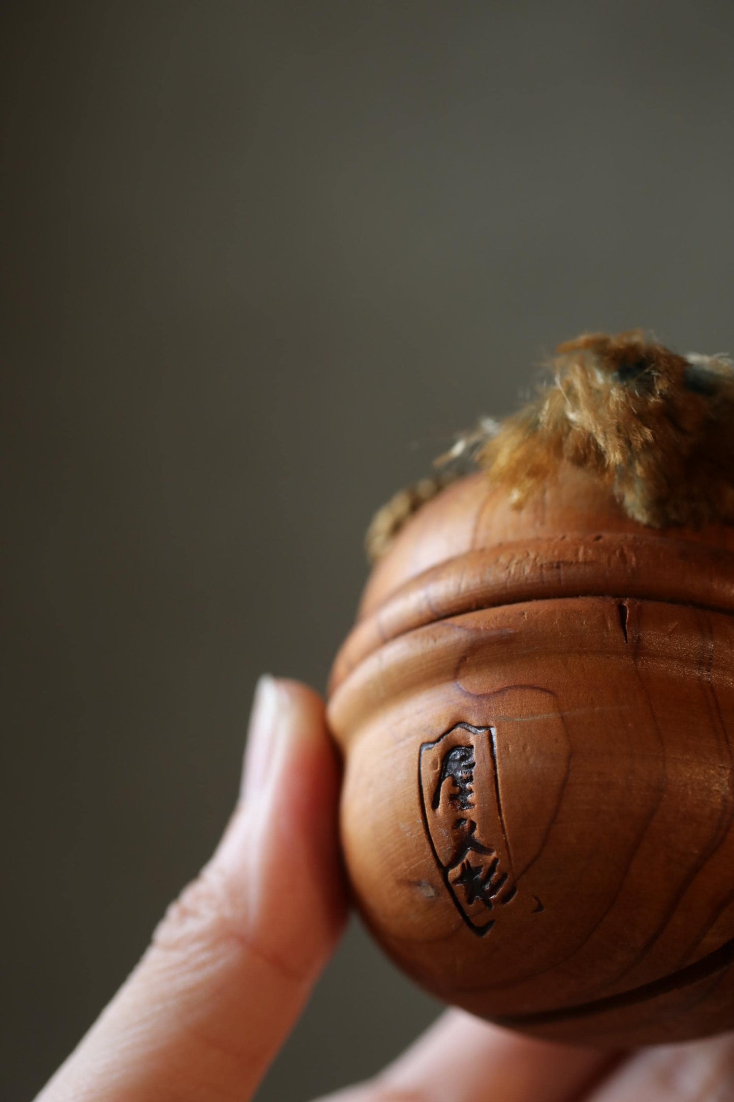 A close-up image of a wooden object, possibly a ball or a piece of furniture, with a hand holding it.