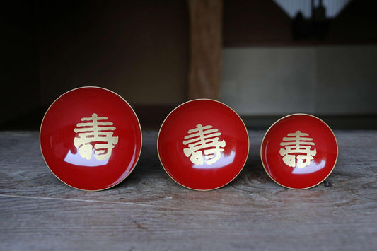 Three red bowls with gold Chinese characters on them are arranged in a row on a wooden surface.
