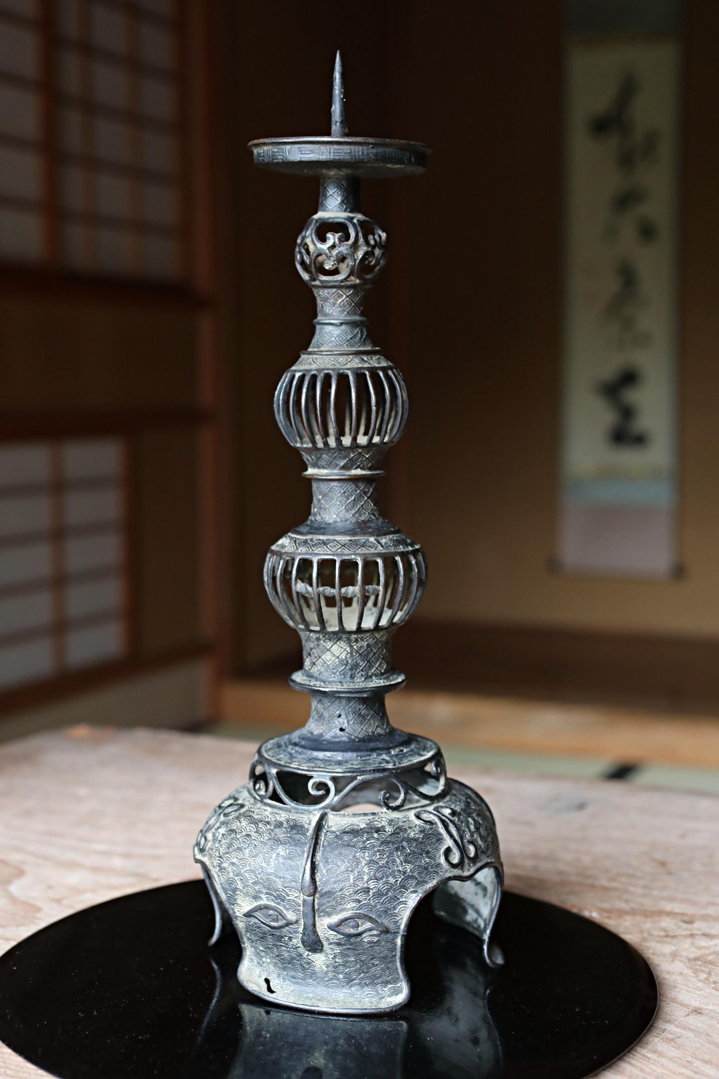 An ornate, antique-looking candle holder with a tall, cylindrical body and a pointed top, sitting on a black circular base.