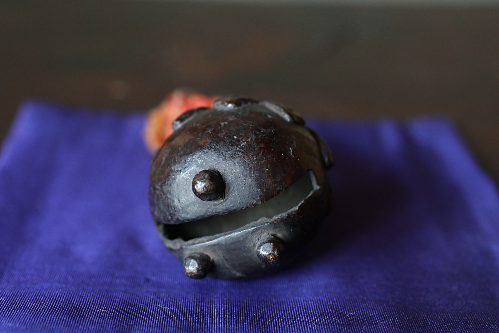 A dark metal bell with a hole in the center, resting on a blue cloth.