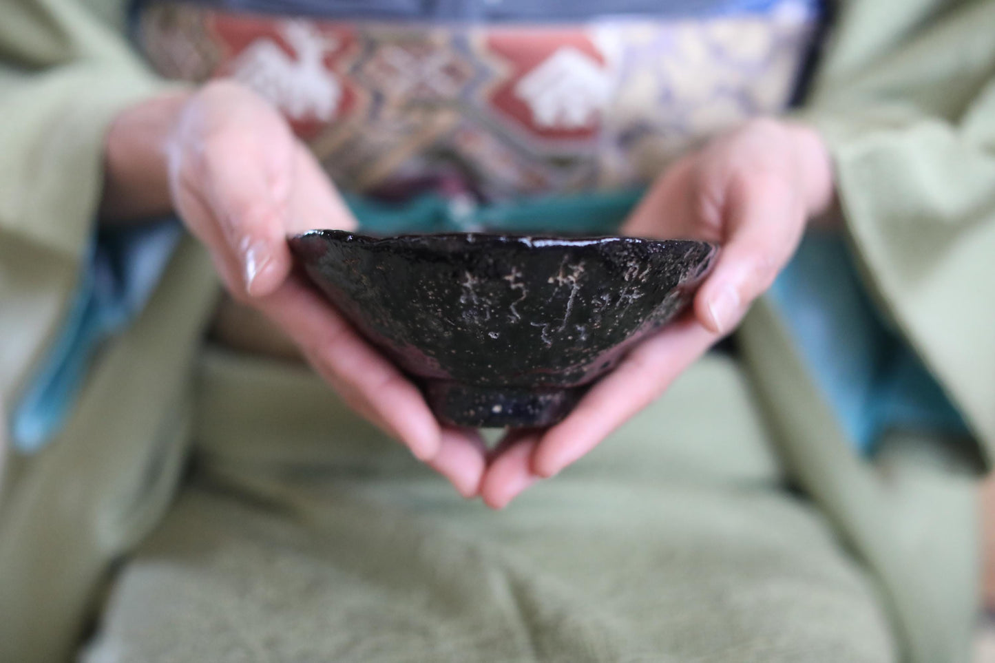 A person's hands holding a small black bowl with intricate designs.