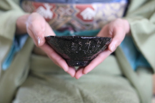 A person's hands holding a small black bowl with intricate designs.