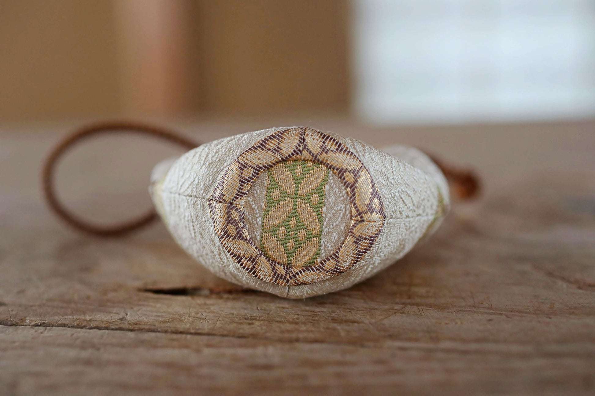 A close-up image of a beige fabric with a decorative pattern, resting on a wooden surface.
