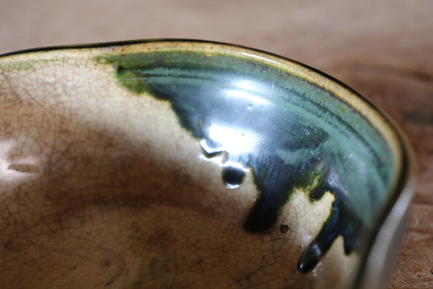 A close-up image of a ceramic bowl with a green and brown glaze, resting on a wooden surface.