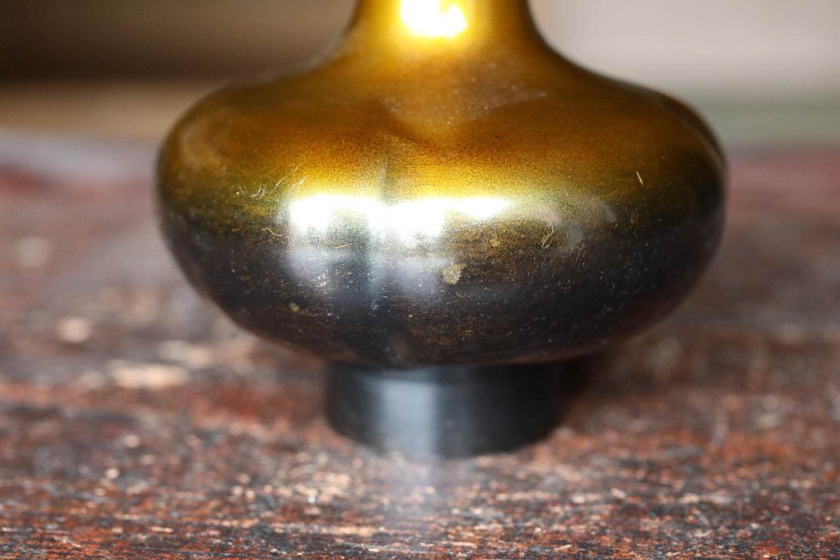 A close-up image of a shiny, golden-colored vase or sculpture with a dark, textured surface.