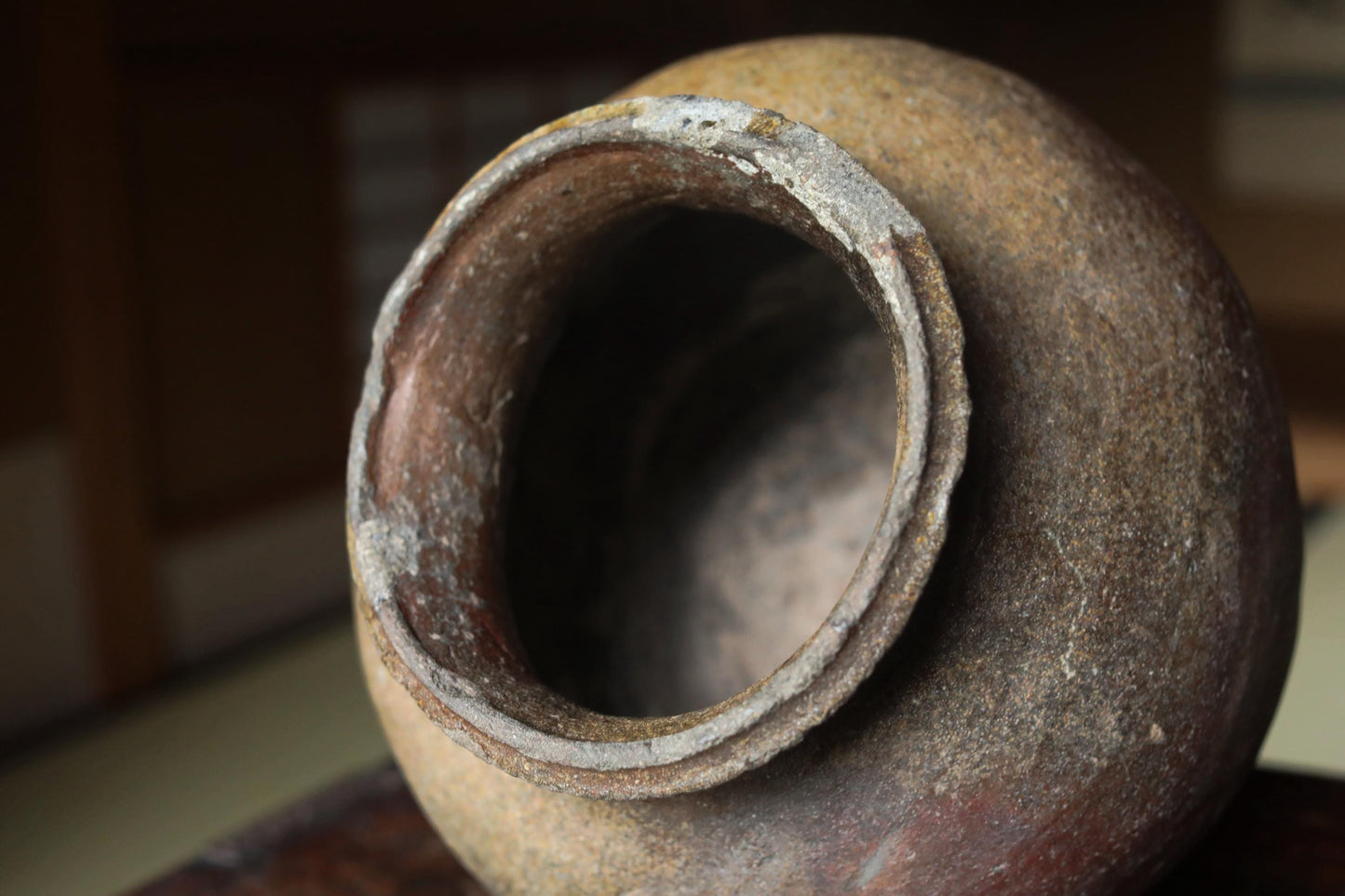 An old, weathered clay pot with a large hole in the center, sitting on a wooden surface.