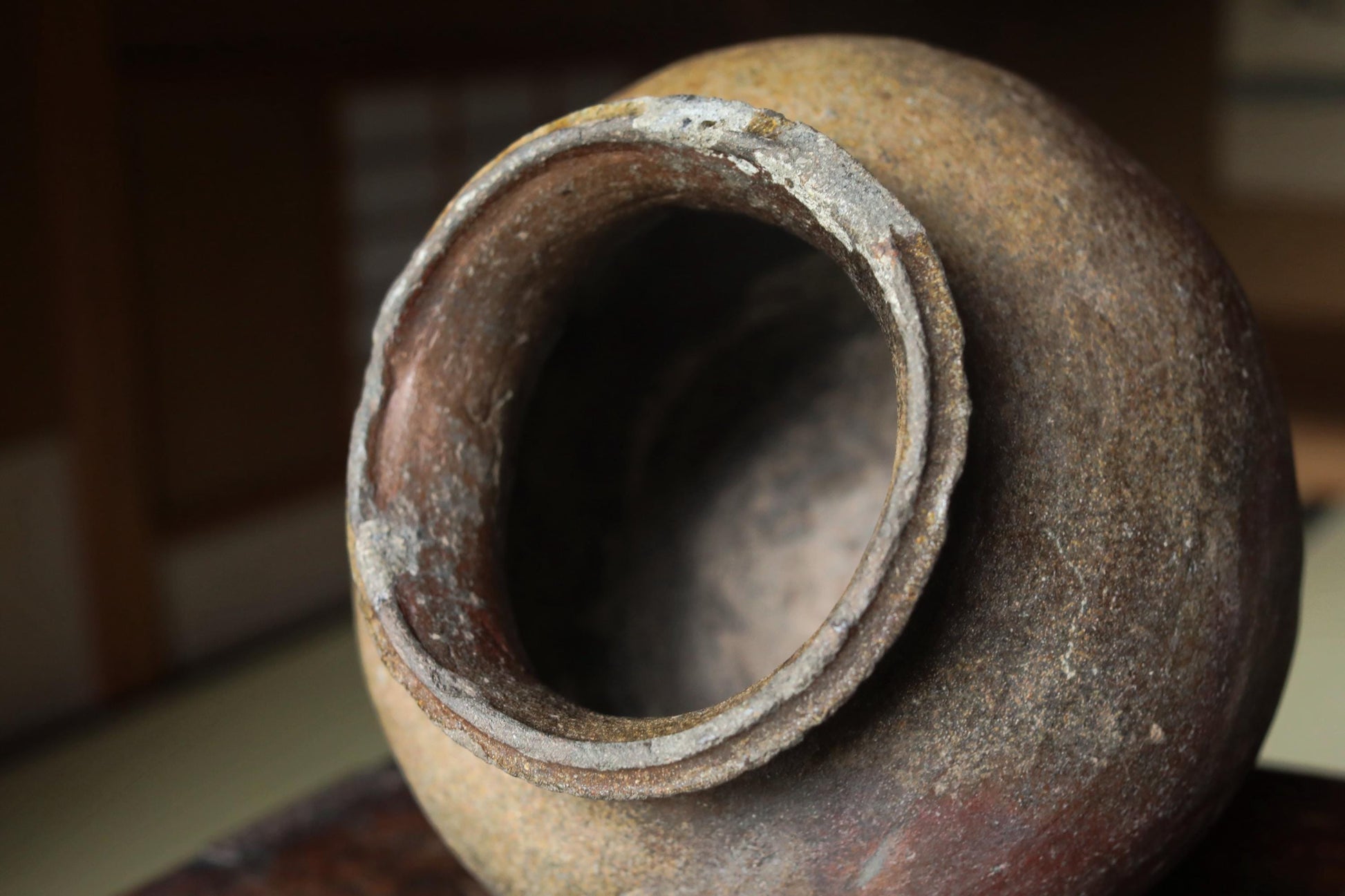 An old, weathered clay pot with a large hole in the center, sitting on a wooden surface.