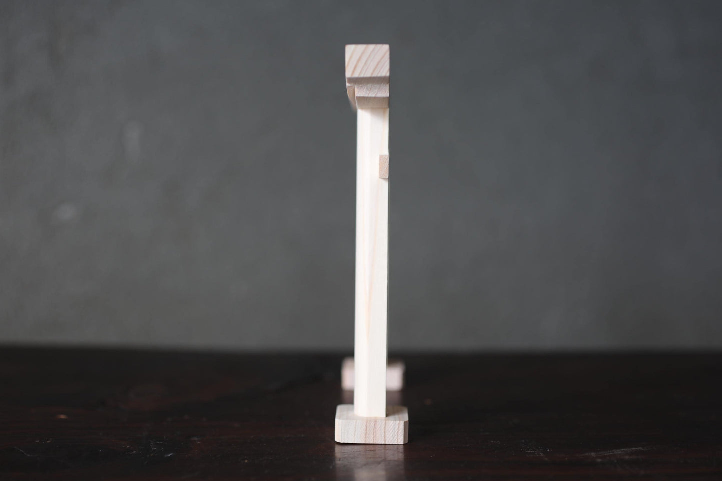 A wooden object, possibly a piece of furniture or a decorative item, is standing upright on a dark surface against a gray background.
