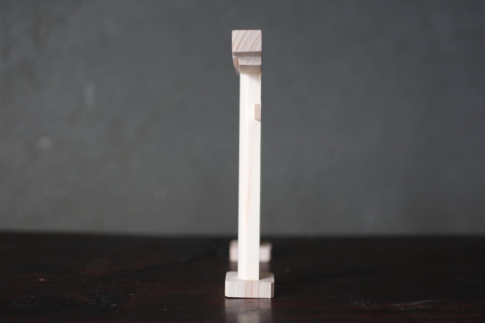 A wooden object, possibly a piece of furniture or a decorative item, is standing upright on a dark surface against a gray background.