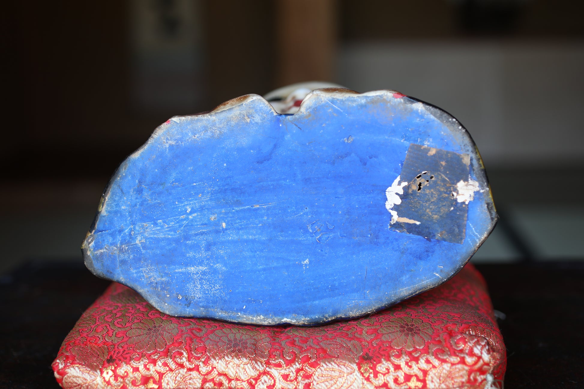 a blue, weathered object with a small hole in the center, resting on a red and gold patterned cushion.