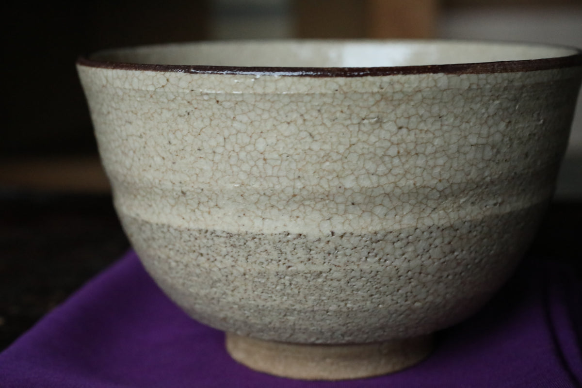 A close-up image of a white ceramic bowl with a textured surface, placed on a purple cloth.