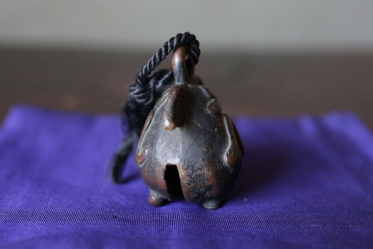 A small, rusted metal bell with a black cord hanging from it, resting on a purple cloth.