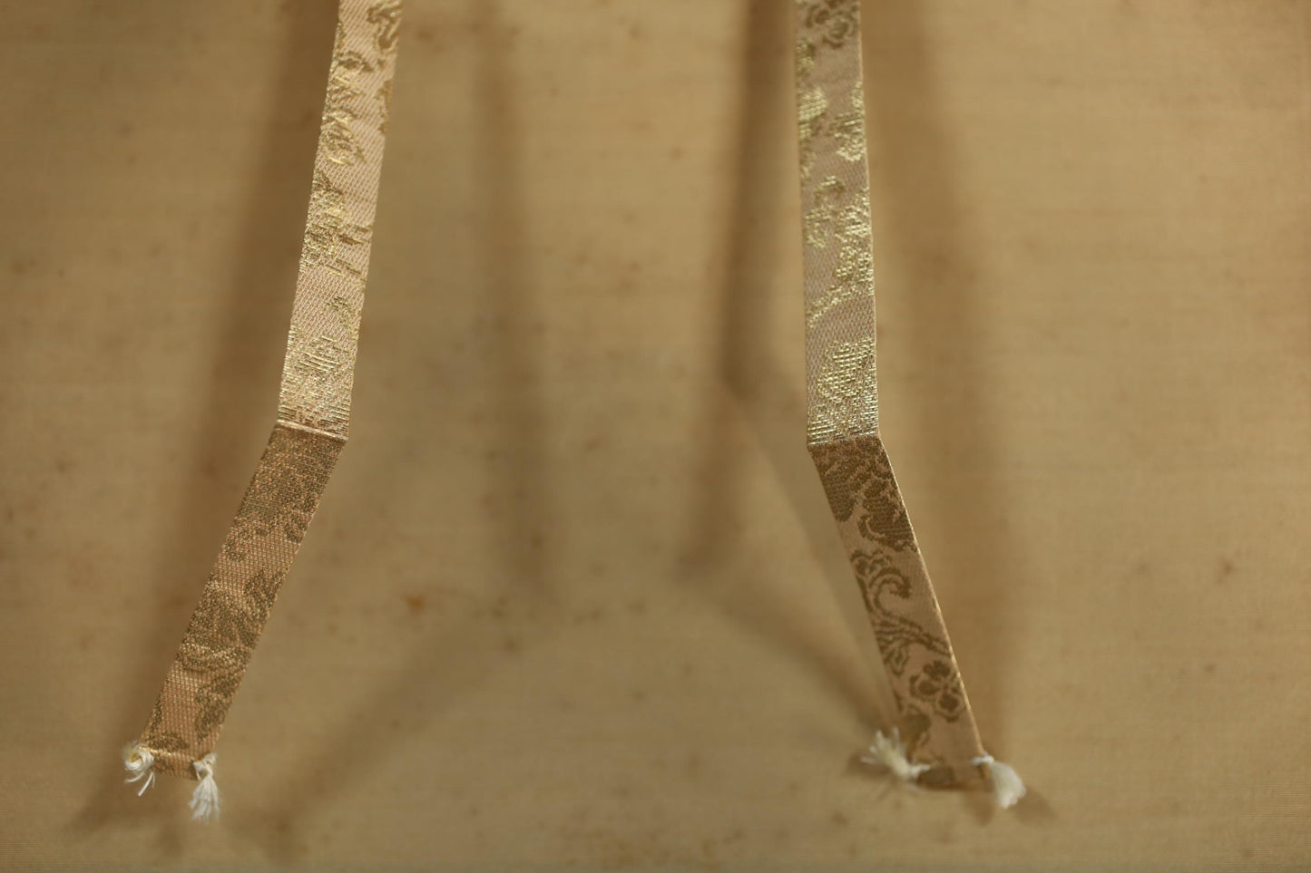 two gold-colored ribbons with a floral pattern, hanging side by side on a beige background.