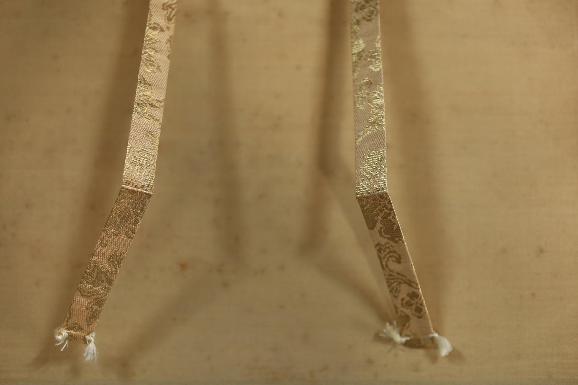 two gold-colored ribbons with a floral pattern, hanging side by side on a beige background.