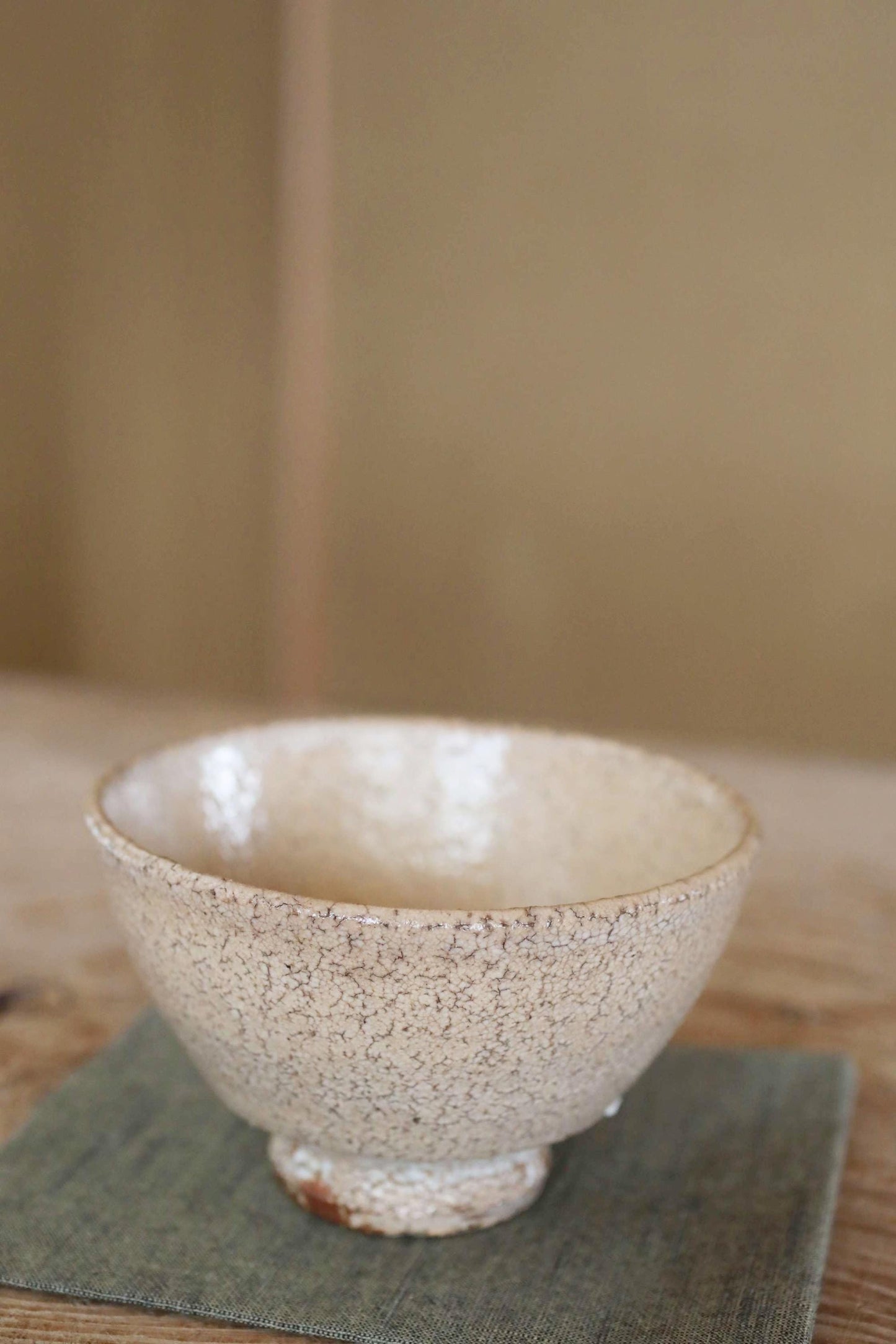 A white ceramic bowl with a speckled texture sits on a green cloth on a wooden surface.