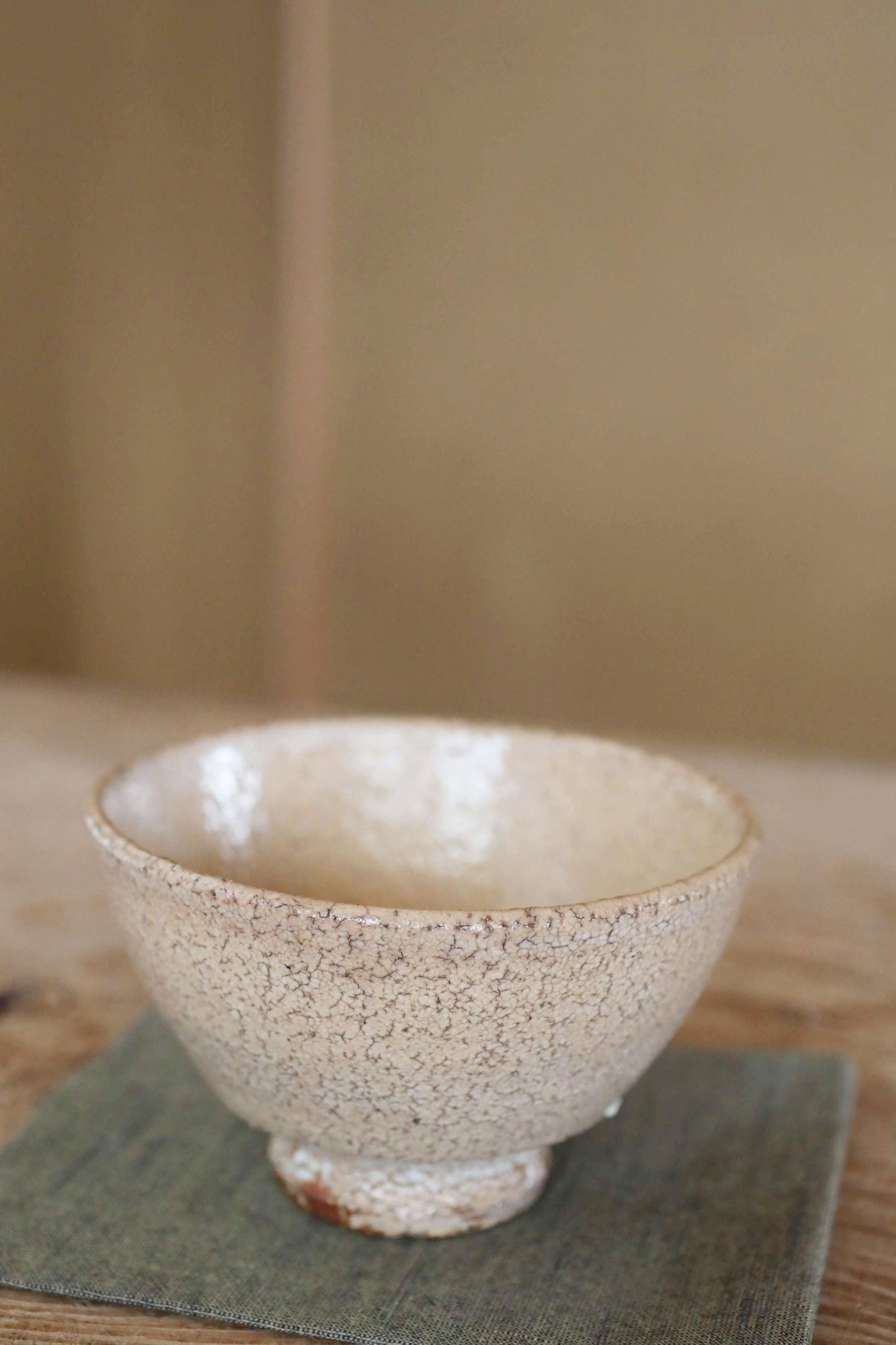 A white ceramic bowl with a speckled texture sits on a green cloth on a wooden surface.