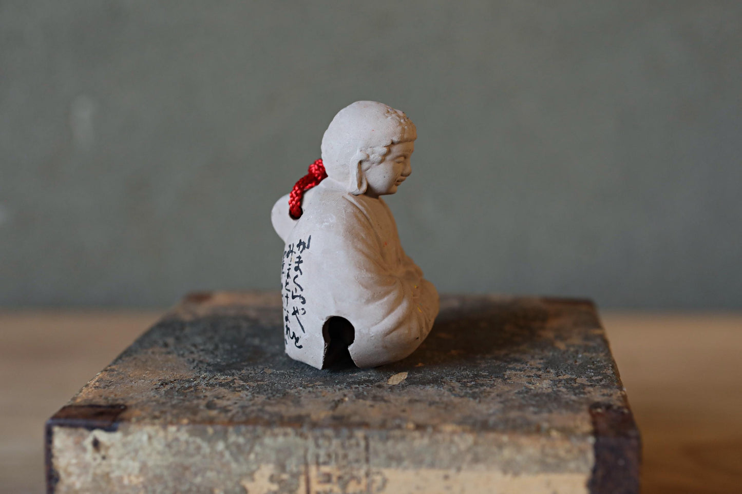 A small white figurine of a person sitting on a wooden surface, with a red ribbon tied around their neck.