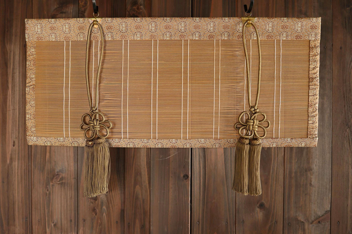 a pair of gold tassels hanging from a bamboo-like material, which appears to be a decorative piece or a wall hanging.