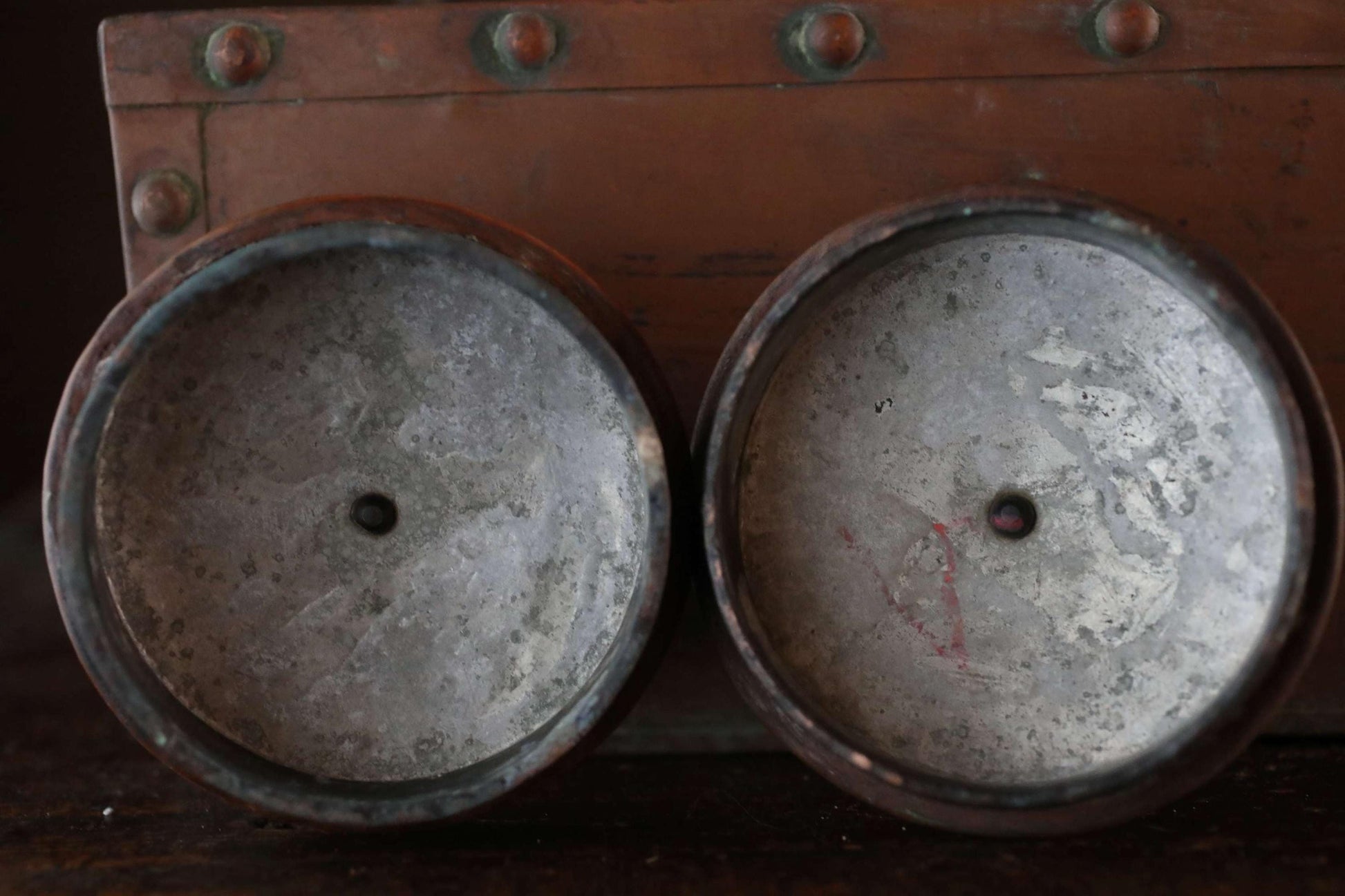 two metal containers with a reddish-brown background, one with a small hole in the center.