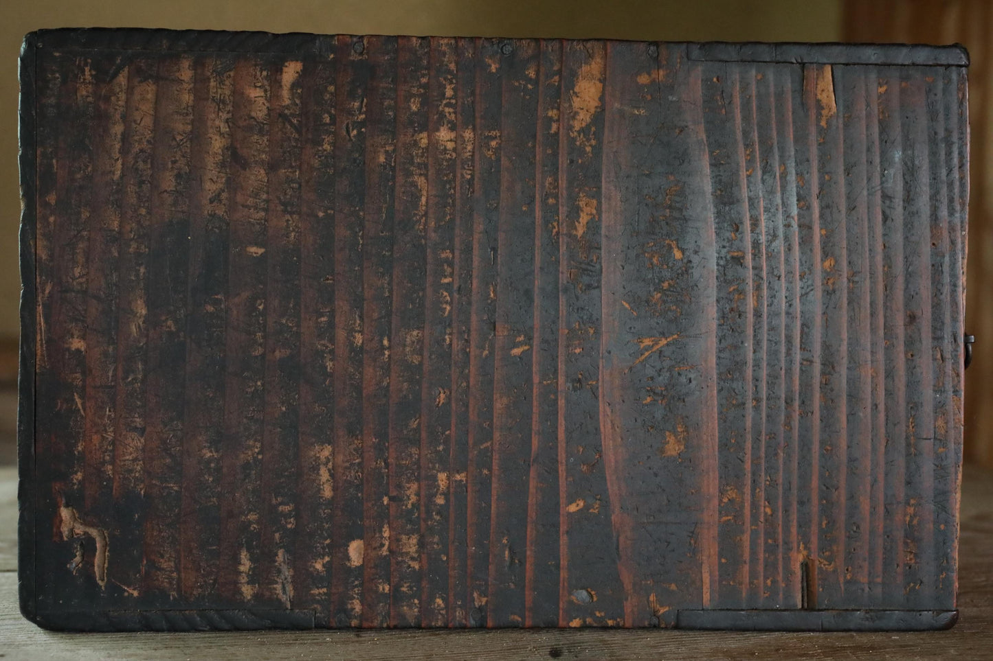 a close-up view of a weathered, dark wooden surface with visible cracks and peeling paint.